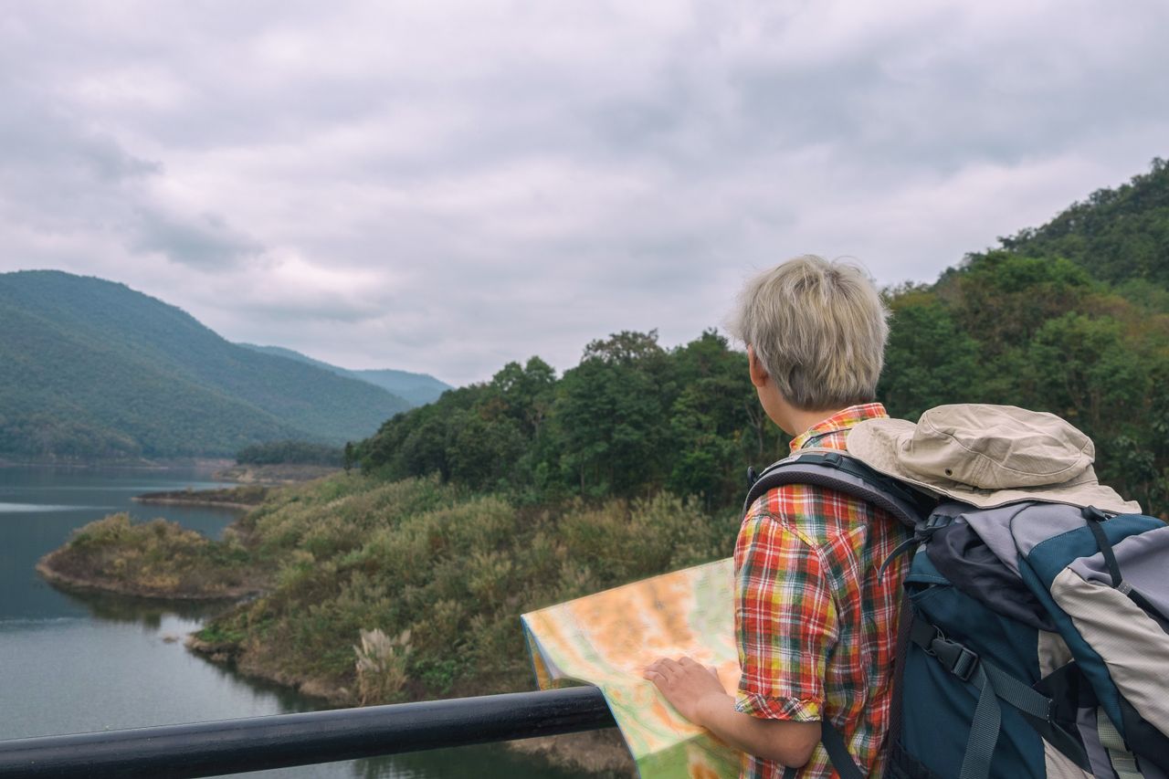 why-choose-us Traveler with backpack and map exploring picturesque mountain landscape.
