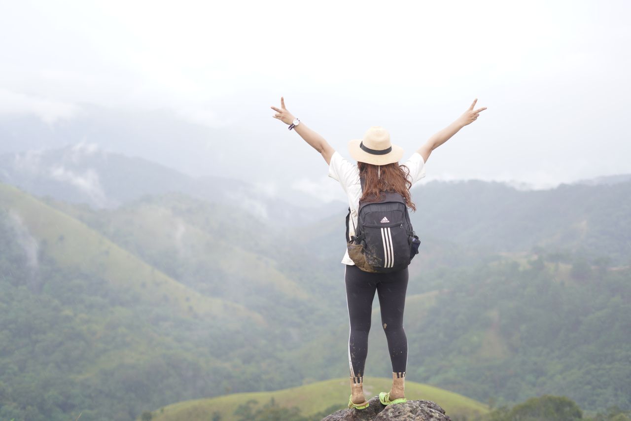 hero-img-02 A woman hiker on a mountain top celebrating the scenic view with open arms.